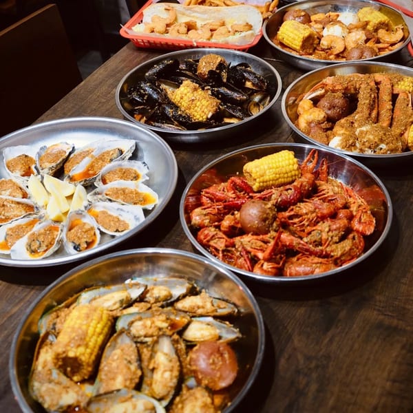 A feast of seafood boils, including oysters, mussels, crawfish, shrimp, and crab, on a wooden table.