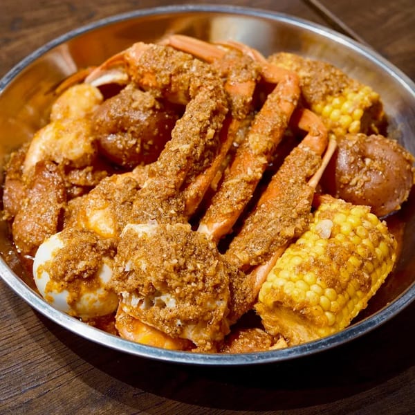 A metal bowl filled with The Pirate's Boil seafood, corn, potatoes, and eggs, seasoned with spices.