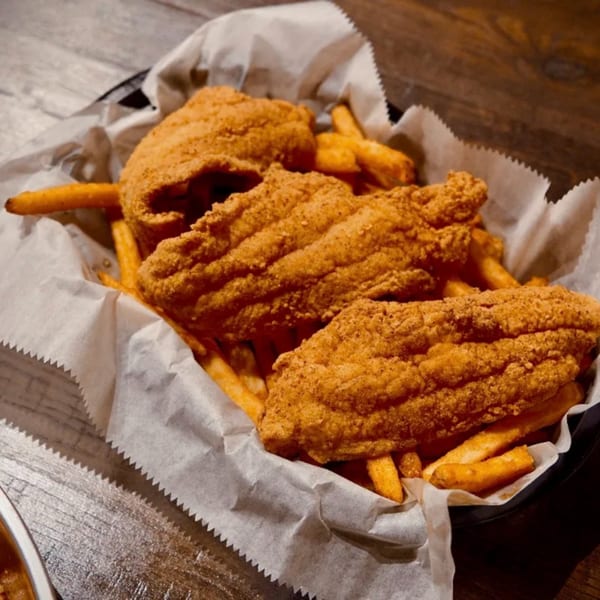 Crispy fried fish and golden french fries served in a basket lined with white paper.