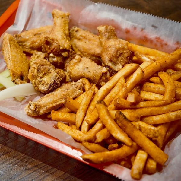 A red basket filled with crispy fried chicken wings, seasoned french fries, and celery sticks.